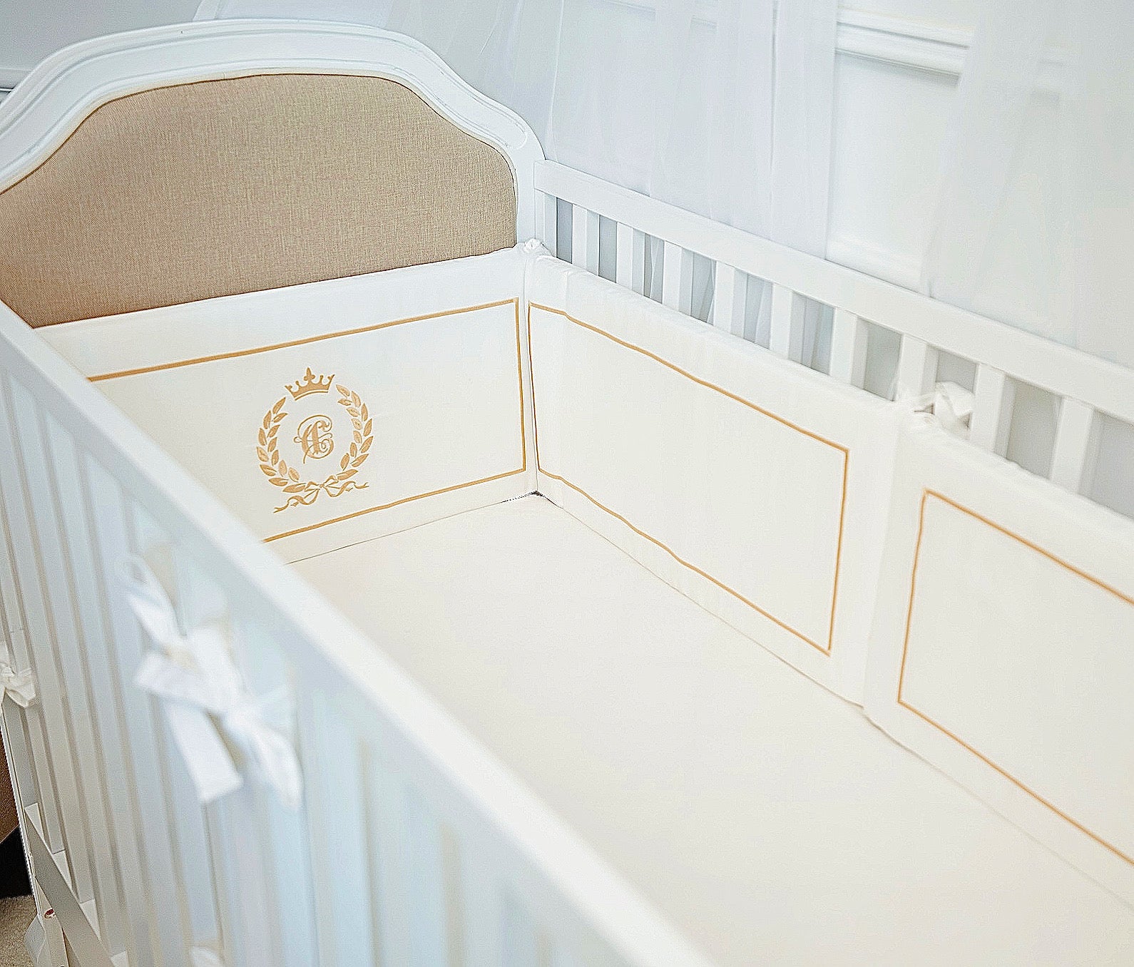 White crib with gold trim and a logo on a white background