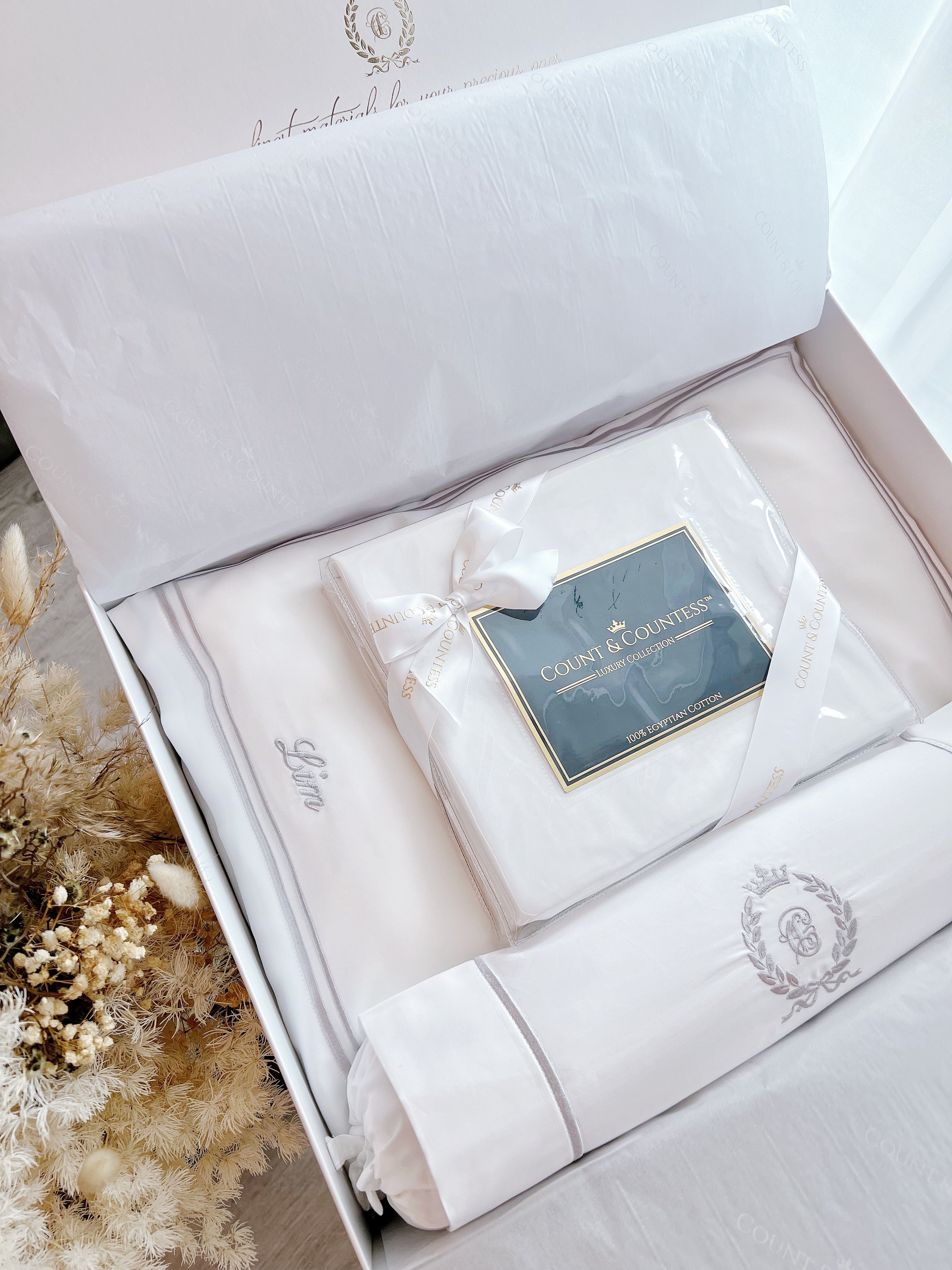 White embroidered baby pillow in a box with a visible brand label, surrounded by decorative elements.