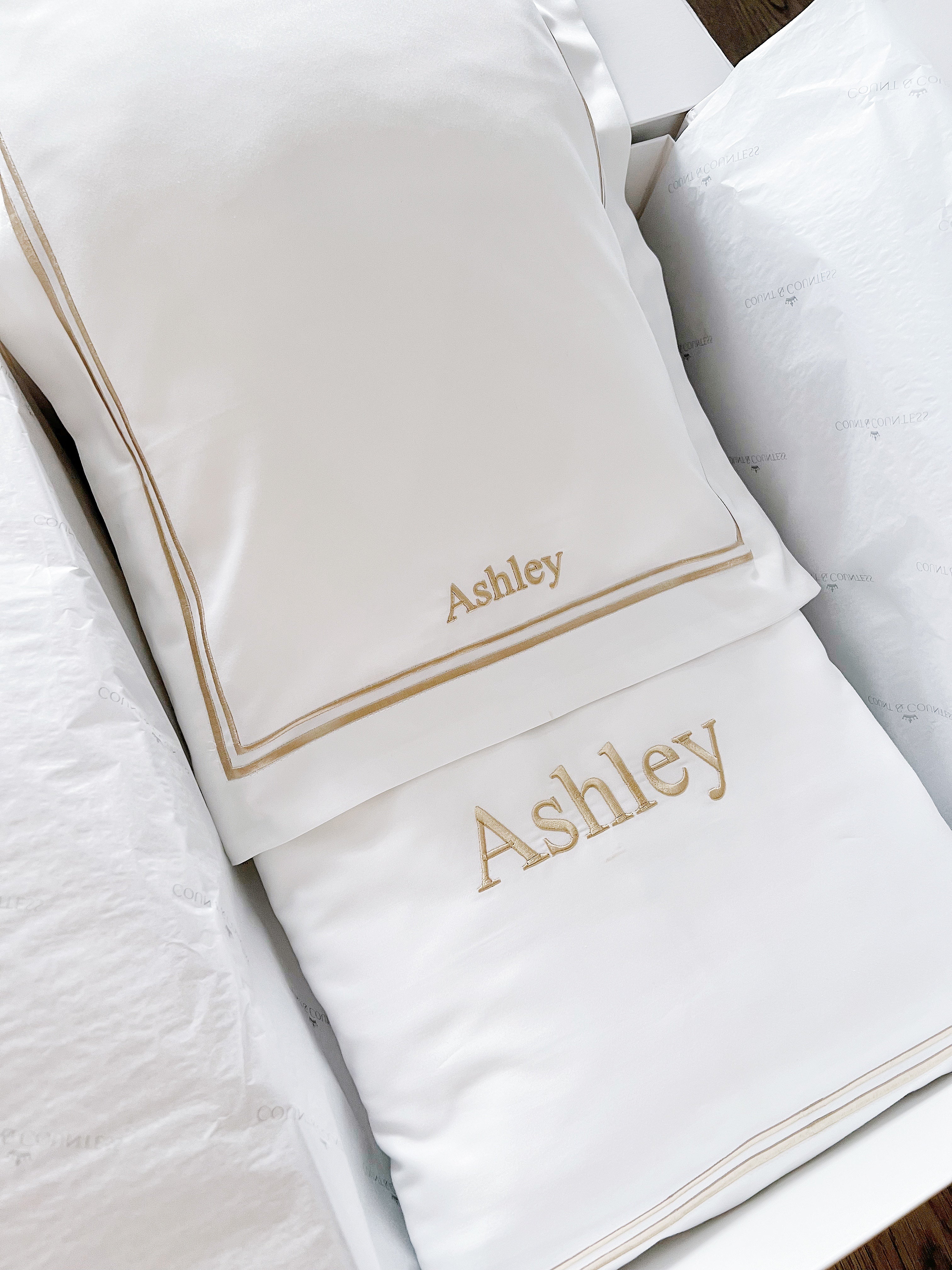 White pillowcases with 'Ashley' embroidery on a bed.