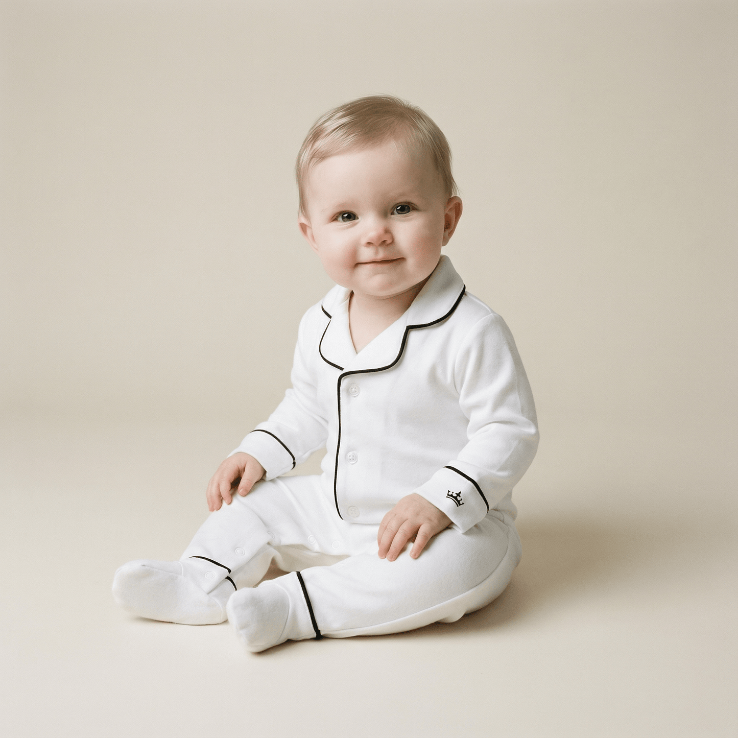 Baby wearing white pajamas with black trim on a beige background