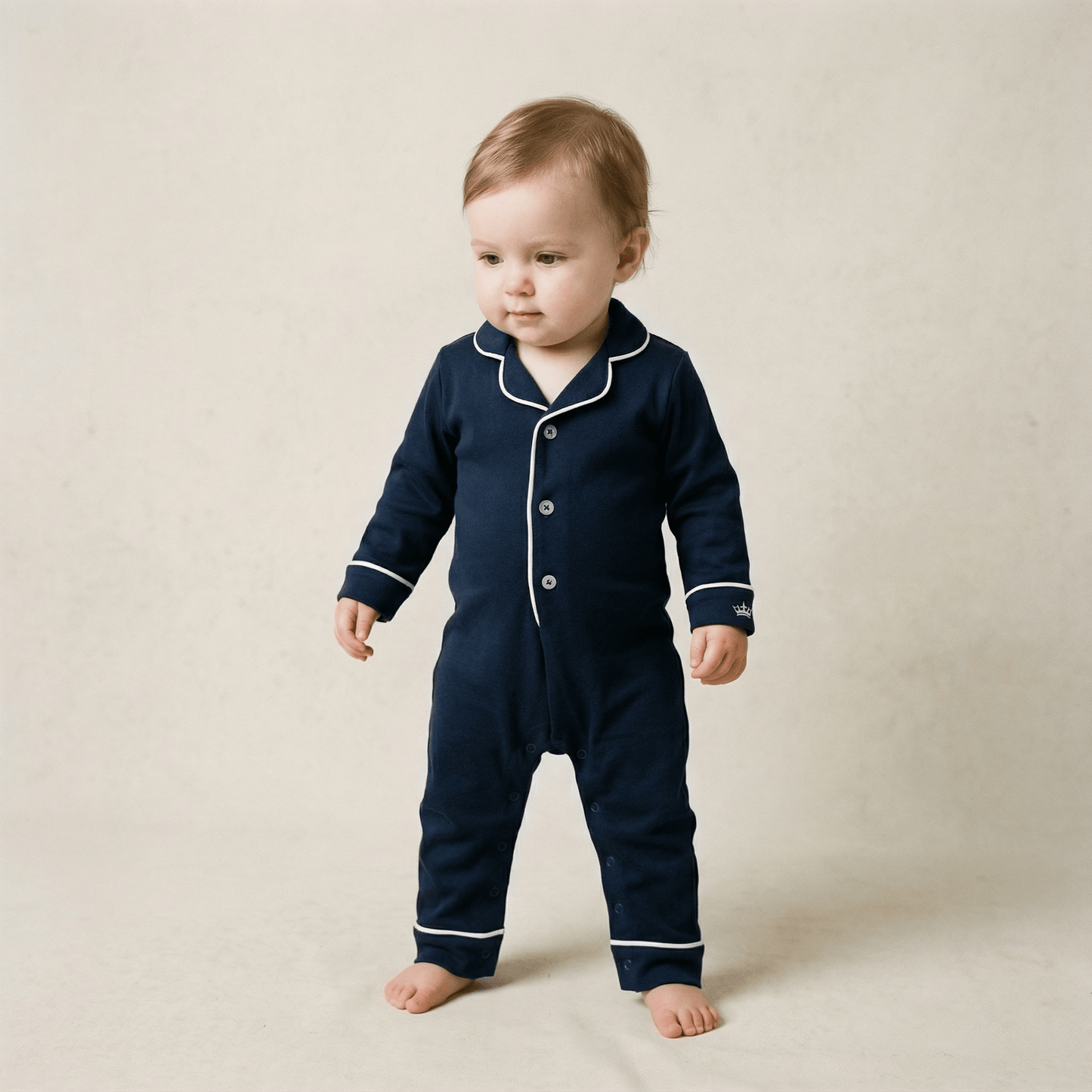 Baby wearing a navy blue pajama set with white trim on a beige background