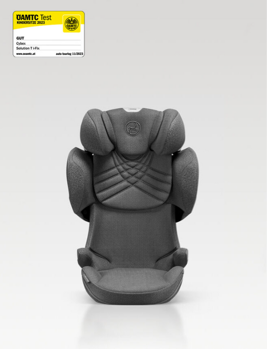 A dark gray textured Cybex Booster child car seat shown from the back, featuring padded headrests, shoulder supports, and a molded harness insert. A small DAMTC Test label is visible in the top-left corner on a light gray studio background.